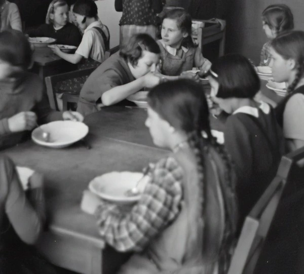 Historical black and white photo of students eating school lunch